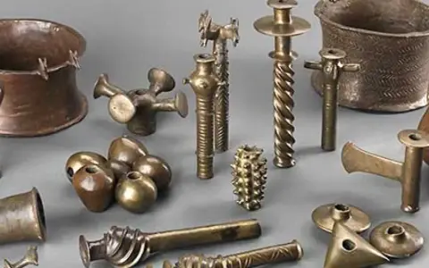 Colección de **herramientas de la edad de los metales**, incluyendo vasijas, soportes y objetos ornamentales de bronce y cobre.