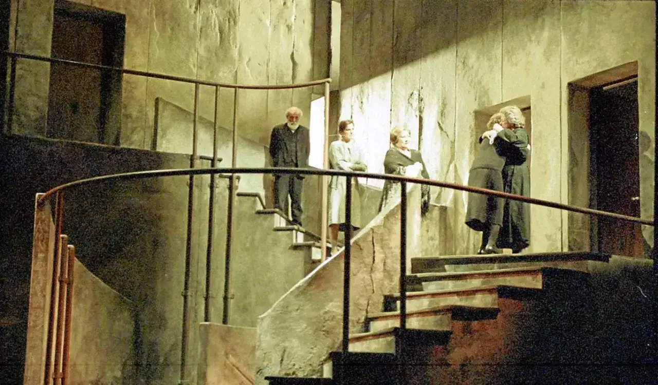 Una escalera de caracol es el escenario de esta historia. Personajes observan, otros se abrazan, en un drama escénico.
