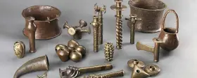 Colección de **herramientas de la edad de los metales**, incluyendo vasijas, soportes y objetos ornamentales de bronce y cobre.