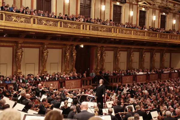 Un director dirige una orquesta sinfónica ante un público entusiasta, interpretando obras de Beethoven en un teatro majestuoso.