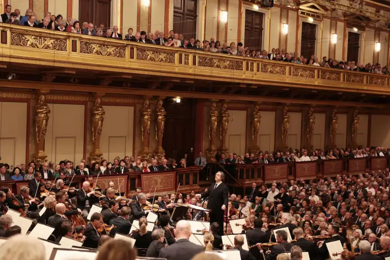 Un director dirige una orquesta sinfónica ante un público entusiasta, interpretando obras de Beethoven en un teatro majestuoso.